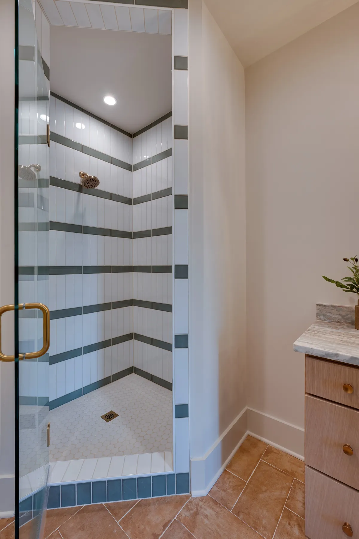A modern, spa-inspired bathroom featuring a glass shower enclosure, striking striped wall tiles, a golden showerhead, and hexagonal floor tiles. The mood is calm and rejuvenating—perfect for self-care routines or unwinding after a long day.