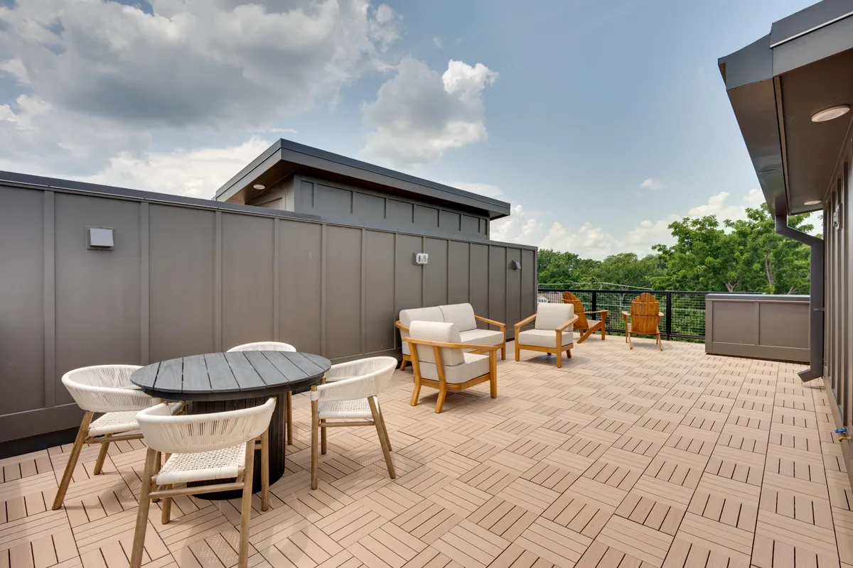 This image showcases an inviting rooftop outdoor seating area surrounded by a lush green backdrop. A stylish table sits at the center, perfect for al fresco dining or evening cocktails. The space exudes a casual, welcoming mood—ideal for relaxing, socializing, and entertaining, with the city skyline visible beyond the greenery.