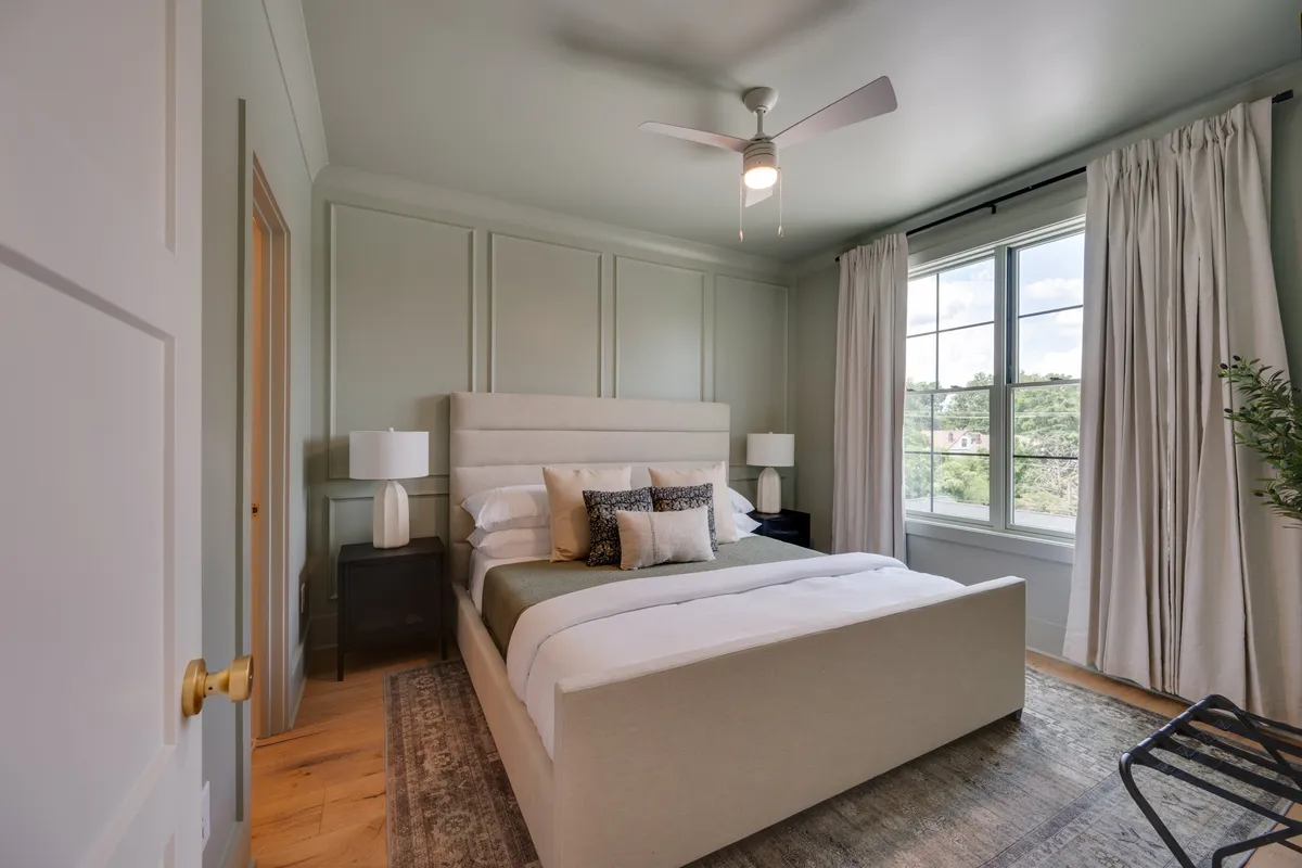 A serene bedroom featuring a plush bed adorned with high-quality linens, flanked by lamps and curtains framing a large window. The space feels calm and private, ideal for unwinding with a book or enjoying quiet moments. The layout and decor emphasize comfort and relaxation.