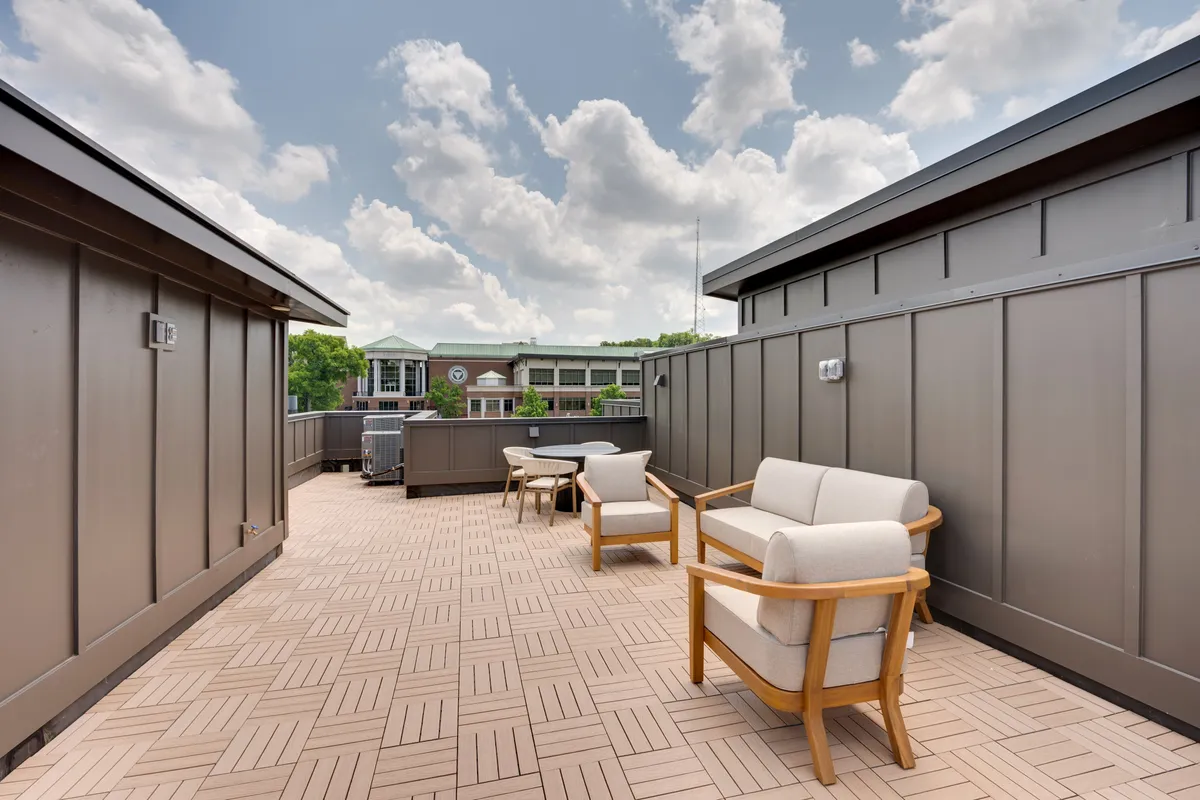 A serene rooftop patio setup featuring wooden chairs, paved flooring, and a broad stretch of sky above. The area is designed for both relaxation and entertaining guests, whether hosting small gatherings or enjoying peaceful moments alone. The open sky suggests opportunities for stargazing or basking in sunshine.