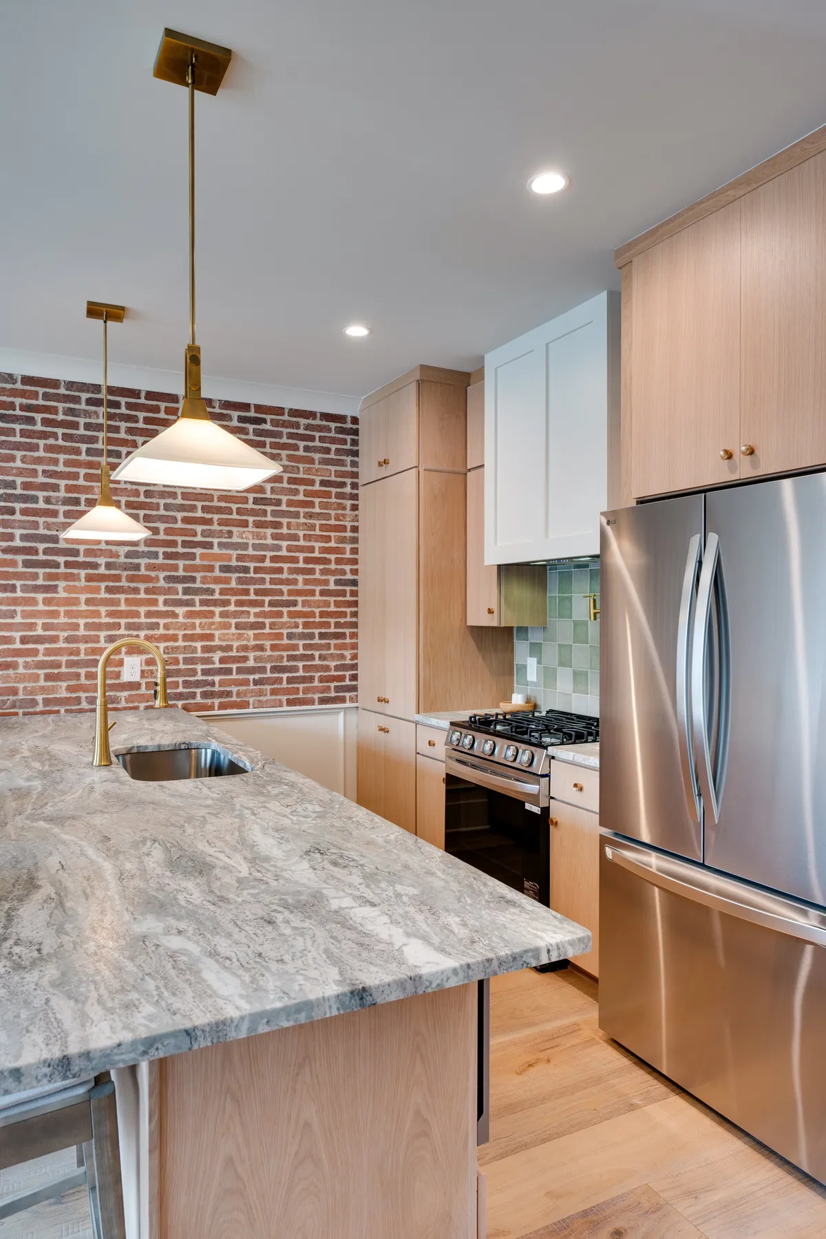 A contemporary kitchen scene featuring a granite countertop, exposed brick wall, modern stainless steel appliances, and elegant gold pendant lights. The space is inviting and functional, with ample counter space and a warm, communal atmosphere perfect for cooking and entertaining.