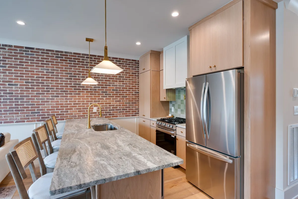 A welcoming kitchen highlighted by a granite countertop, exposed brick wall, hanging pendant lights, and stainless steel appliances. The space is designed for cooking, entertaining, and enjoying meals together, creating a warm, sophisticated atmosphere.