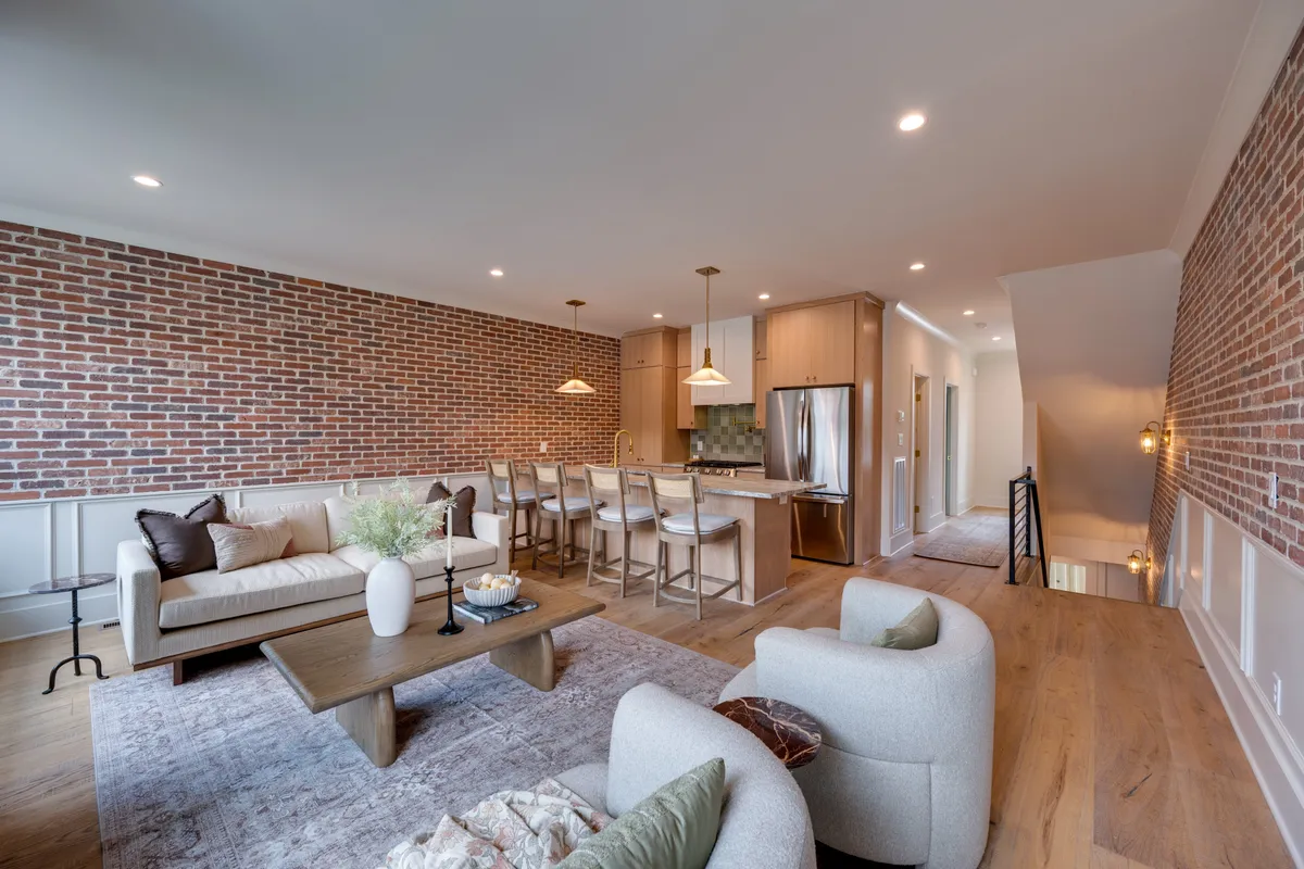 An open-concept interior showcasing an exposed brick wall, a kitchen island, and a comfortable seating area. The layout encourages entertaining, group dining, and relaxed conversation, with views of both the kitchen and living area.