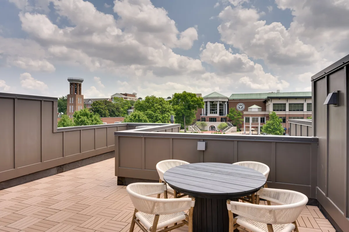 A rooftop seating area with a distant clock tower in view. Surrounded by greenery, the setup encourages relaxed social gatherings, and offers a sense of privacy in a city setting. The scene is bathed in natural light, creating an open, airy atmosphere ideal for enjoying the outdoors while still being connected to the urban landscape.